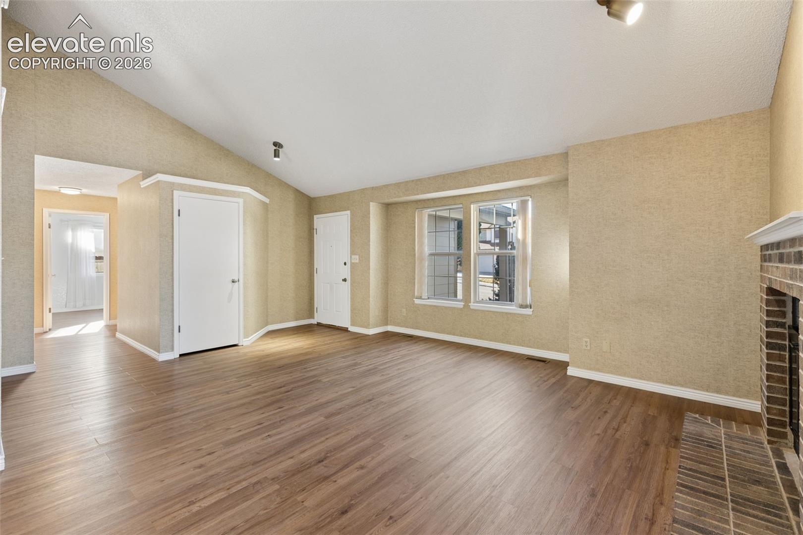 Vaulted ceilings, wood-finish flooring, brick fireplace hearth, and multi-pane windows