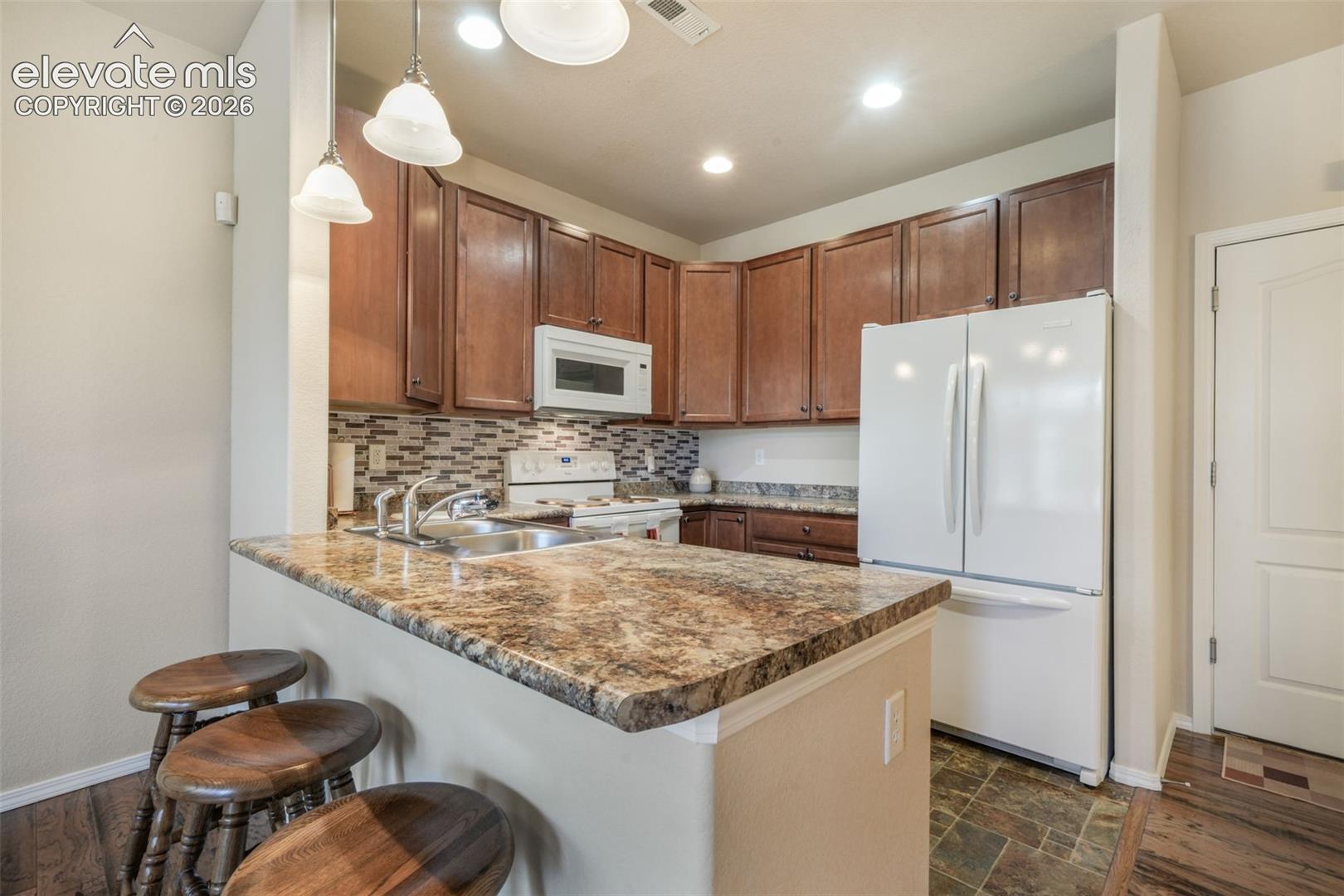 Kitchen featuring a breakfast bar with stone-look countertop, wood cabinetry, tile backsplash, and stainless steel sink