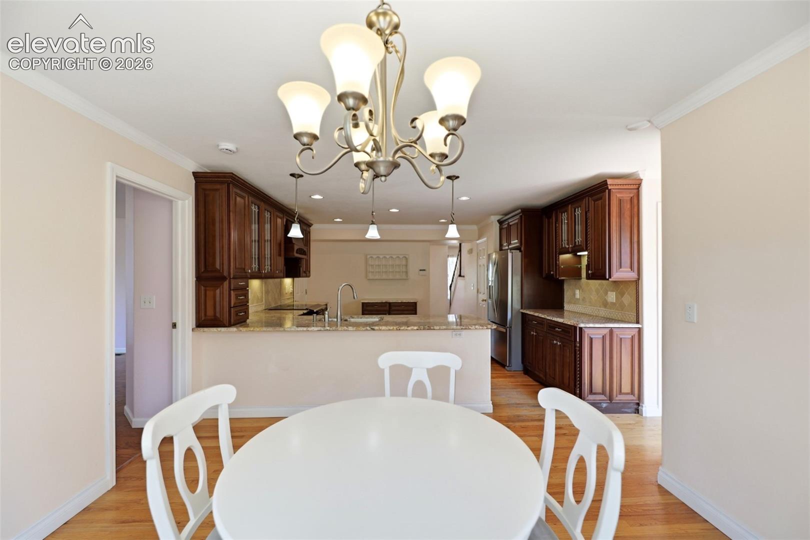 Dining area featuring a chandelier with frosted glass shades, hardwood flooring, and crown molding
