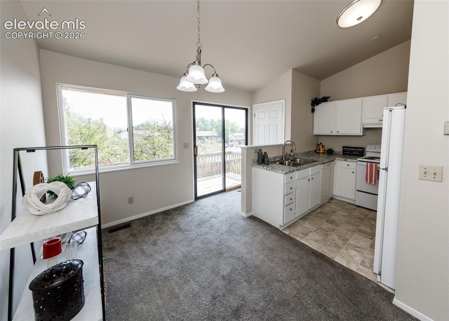Kitchen and dining area featuring white cabinetry, light-toned countertops, a stainless steel sink, and a sliding glass door to an exterior deck