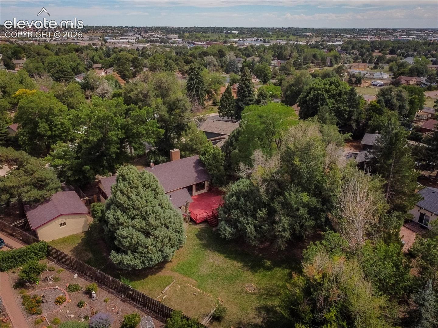 Expansive property featuring lush mature trees, a red deck, a detached shed, and a fenced perimeter