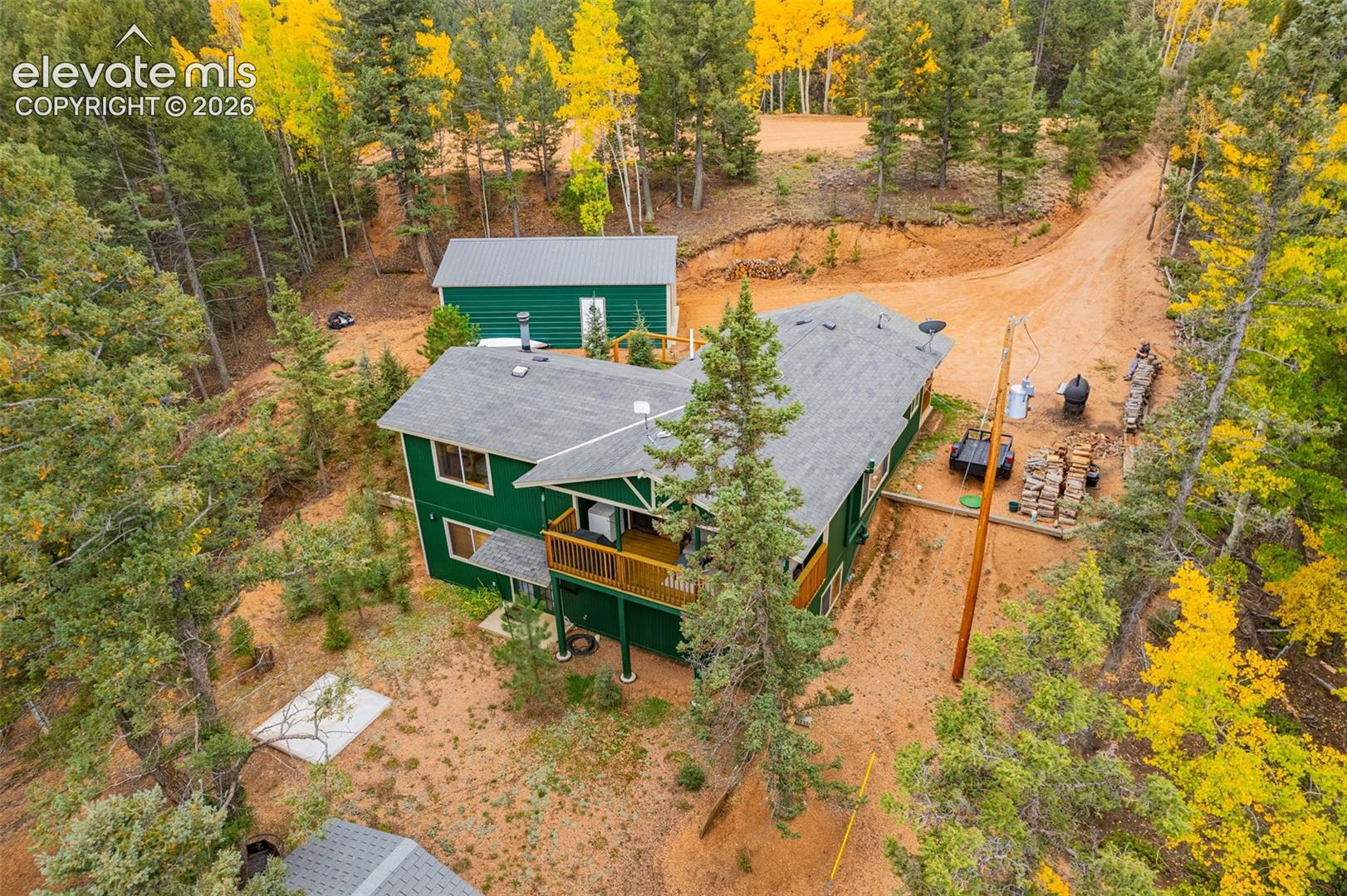 Two-story residence featuring green horizontal siding, shingle roofing, a wood-railing balcony, and a detached outbuilding, all situated within a wooded lot