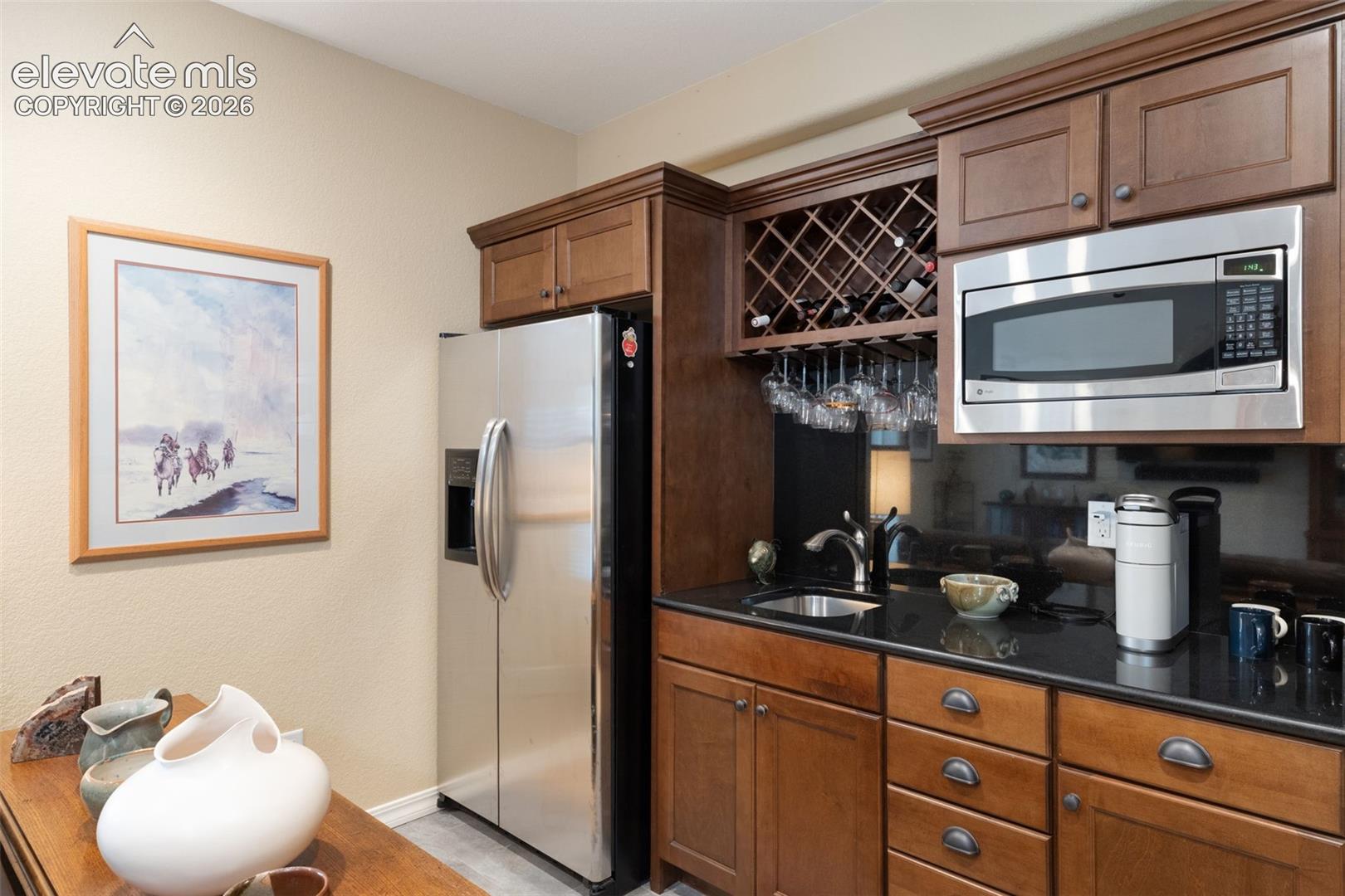 Wet bar featuring a stainless steel microwave, built-in wine rack with stemware storage, undermount sink, and marble countertops