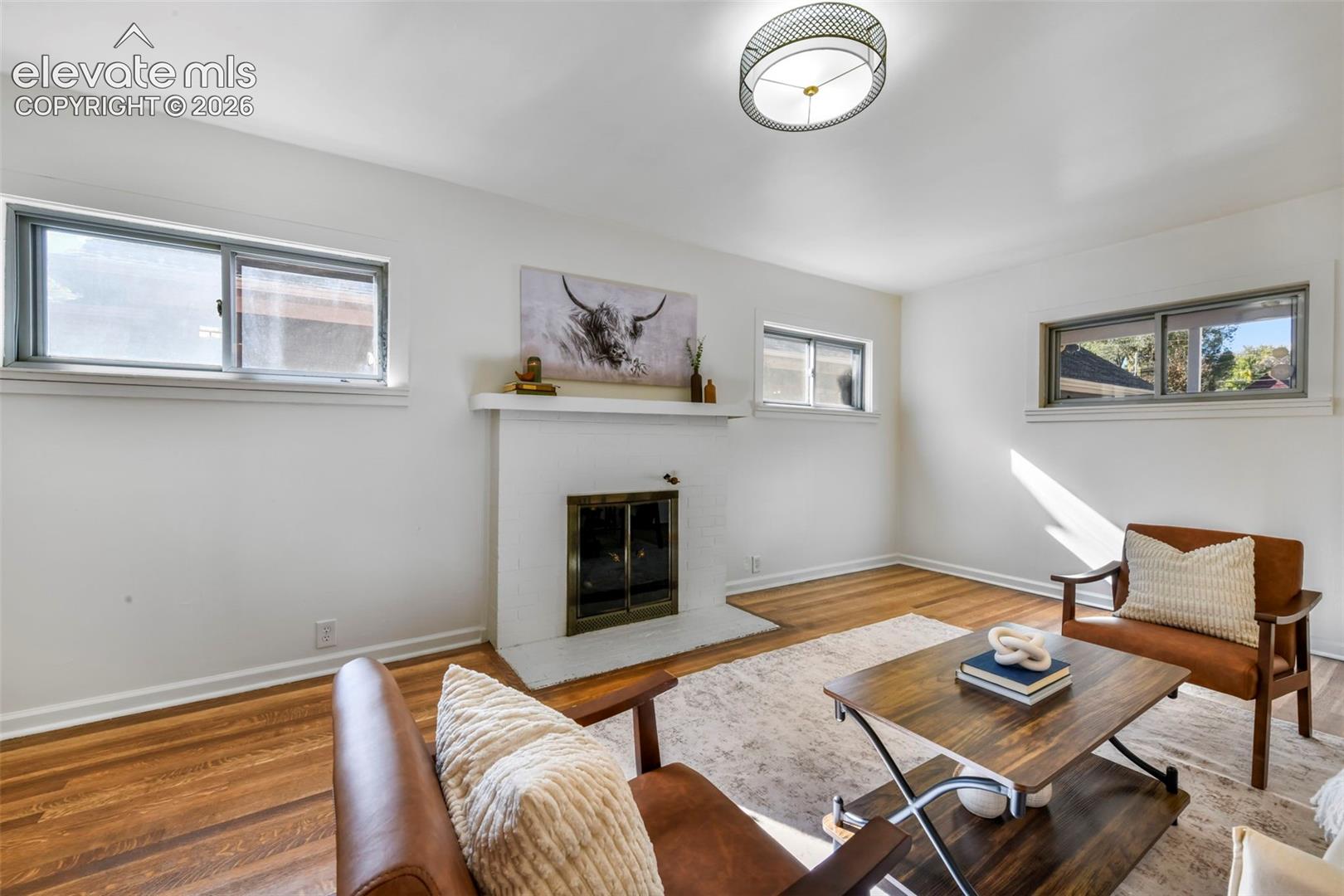 Interior space featuring wood-finish flooring, a painted brick fireplace with a mantel, multiple sliding windows, and a flush-mount drum ceiling fixture