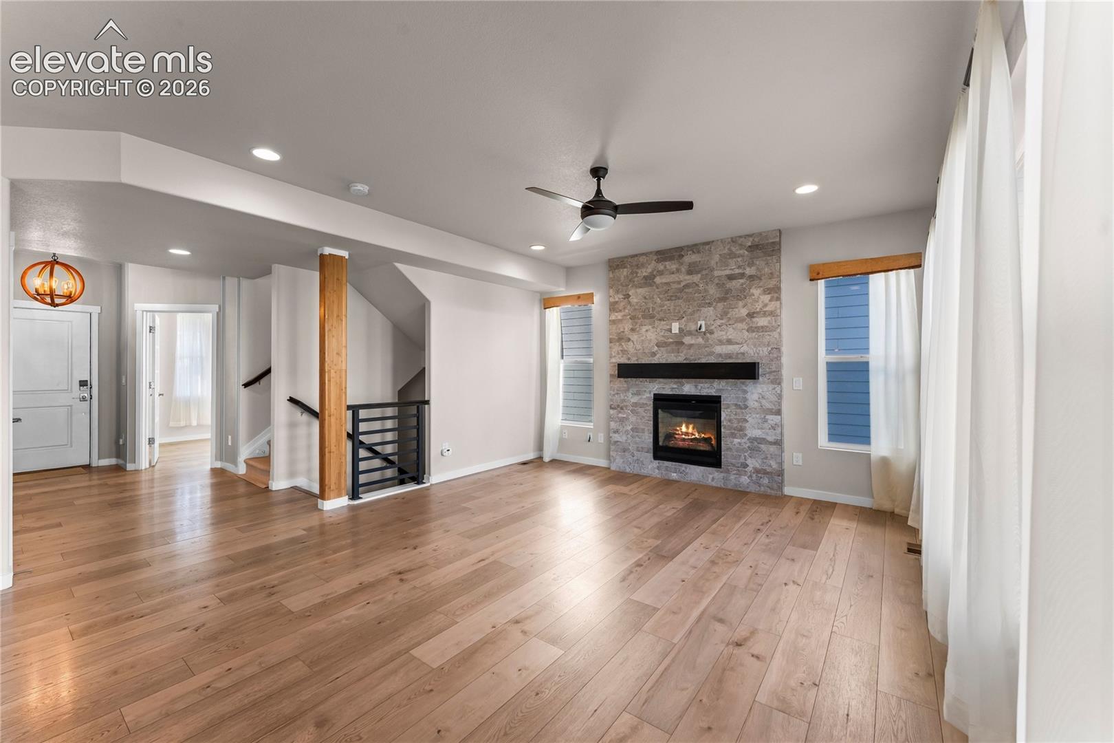 Stone-clad fireplace with a horizontal mantel, wood-finish flooring, ceiling fan, and prominent structural wood post