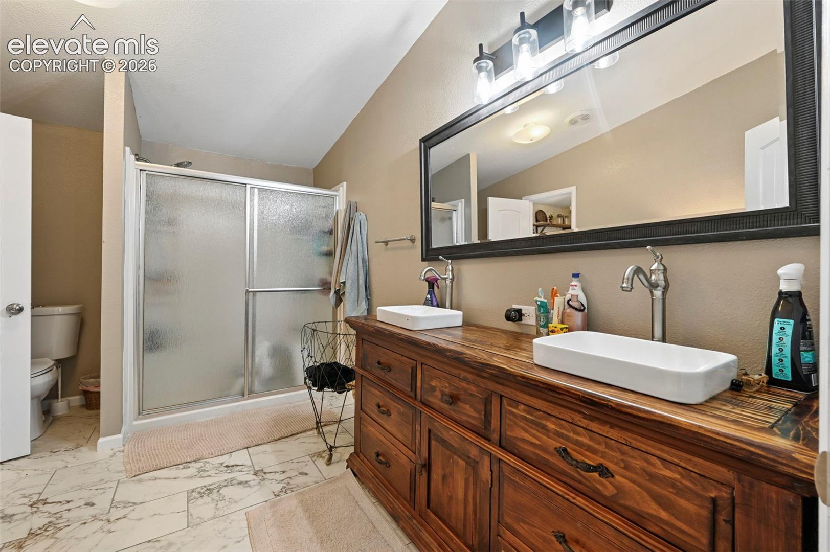 Dual-sink vanity with wood cabinetry, rectangular vessel sinks, matte-finish gooseneck faucets, large framed wall mirror, and floor tiling