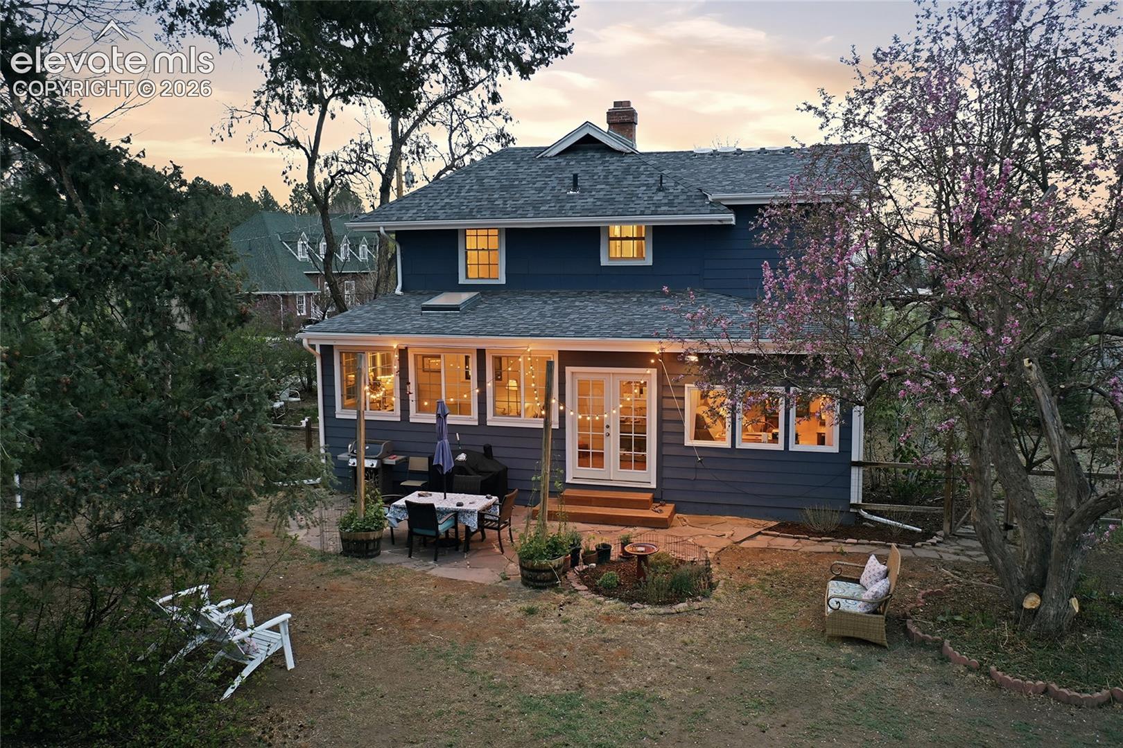 Two-story residence featuring horizontal lap siding, a pitched shingle roof, a stone patio, and French doors