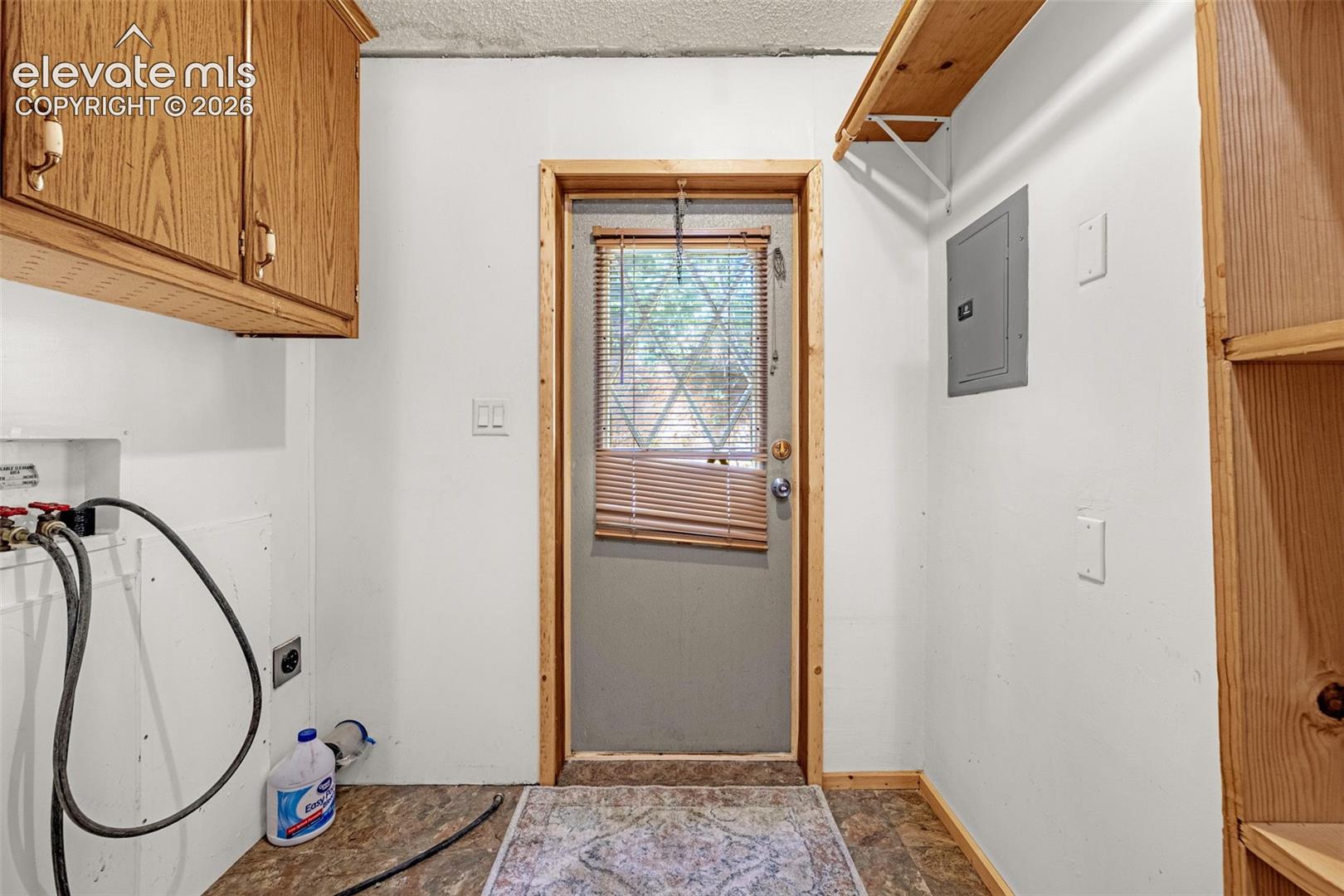 Laundry area featuring wood-finish cabinetry, built-in shelving, and a utility door with integrated blinds