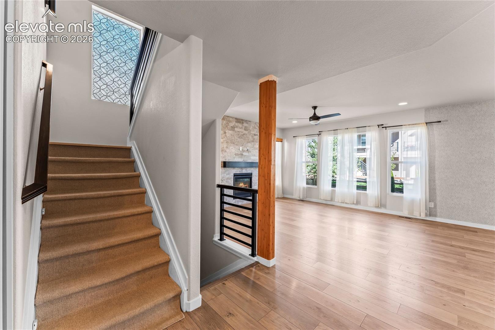 Wood-finish flooring, stone-veneer fireplace, decorative geometric skylight, vertical timber support post, and black metal stair railing