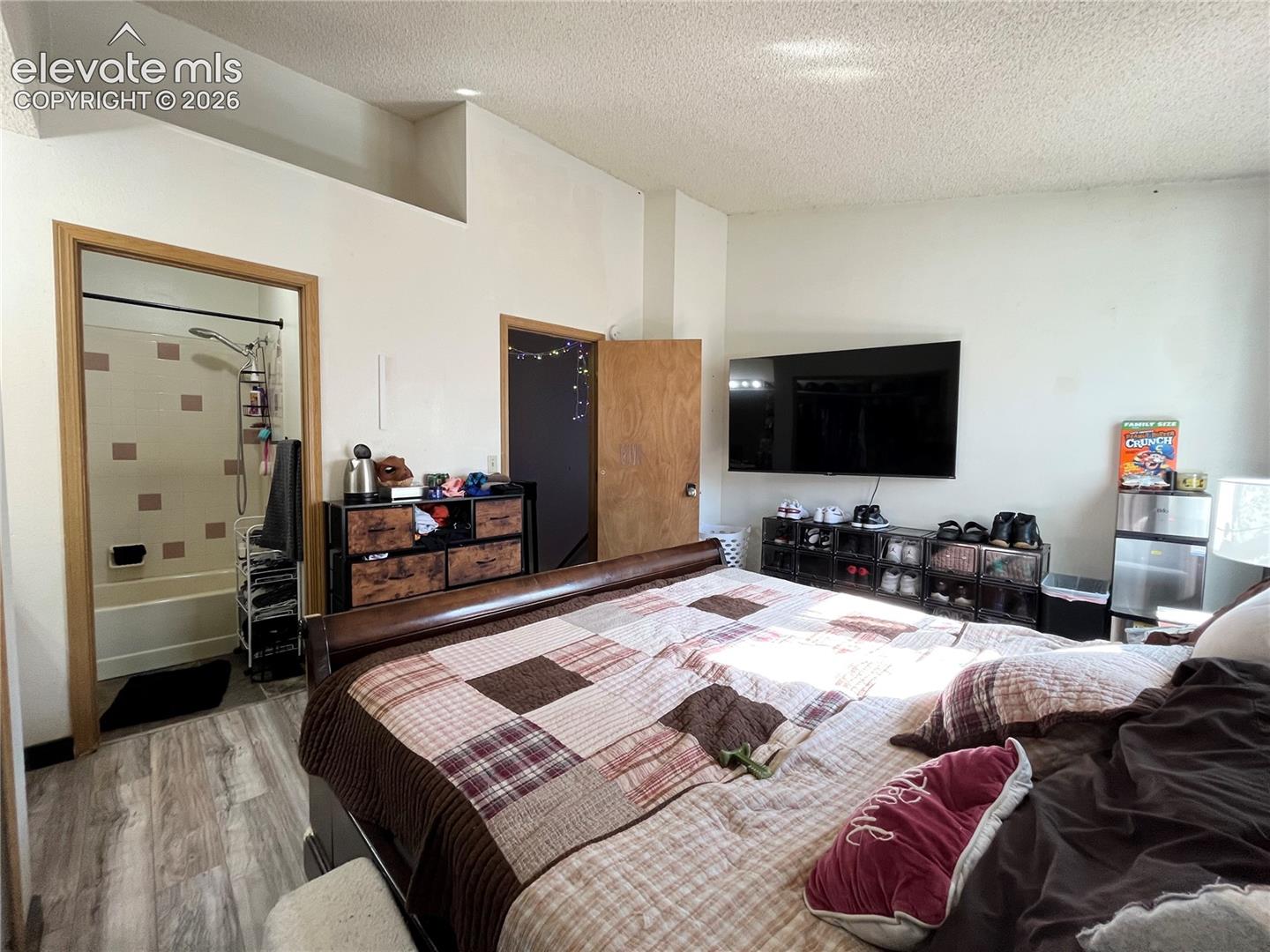 Room featuring wood-finish flooring, vaulted ceiling, and an en suite bathroom with a tile-surround tub