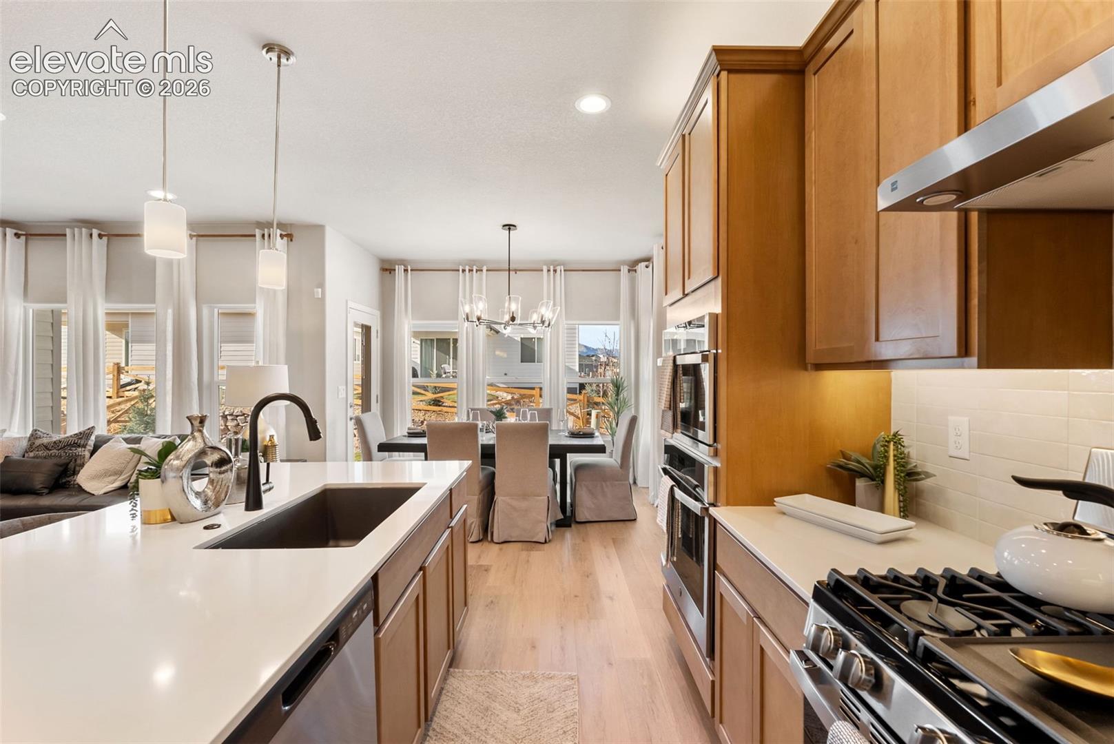 Kitchen featuring quartz countertops, wood cabinetry, built-in double wall ovens, a gas cooktop with stainless steel vent hood, and an undermount sink with a matte black faucet