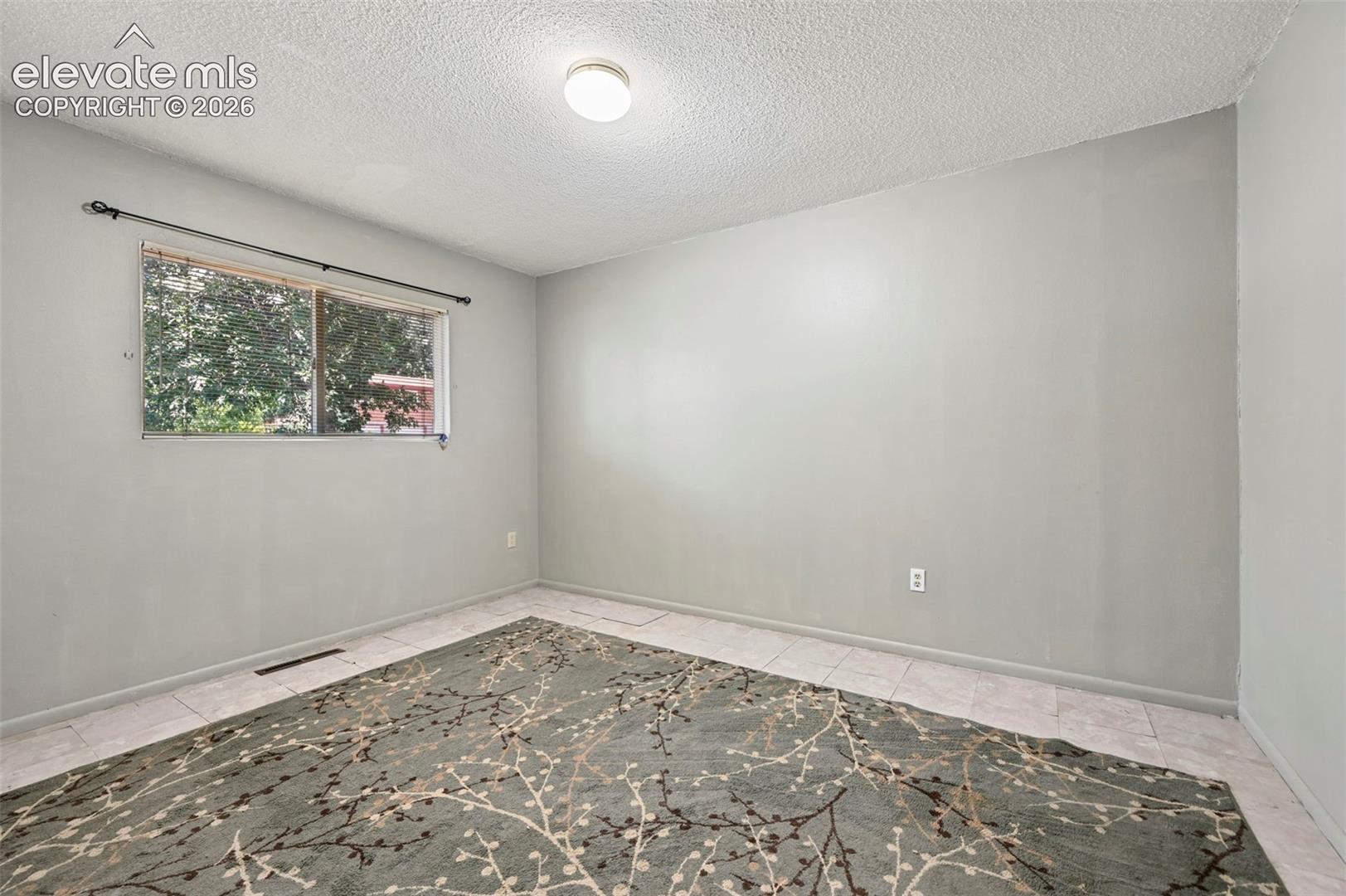 Interior room featuring light gray walls, a single window with a black curtain rod, white baseboards, and light-toned tile flooring