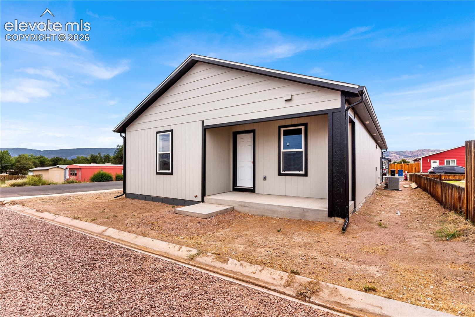 Single-story exterior featuring neutral-toned horizontal siding, a covered front entryway, contrasting black trim, and a concrete porch pad