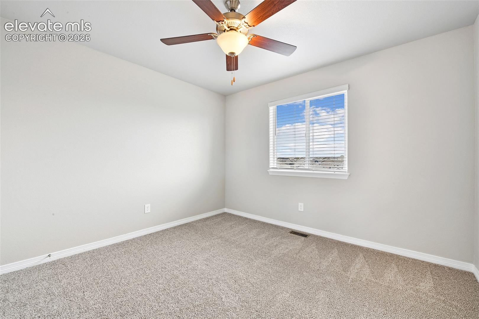 Neutral-toned interior featuring wall-to-wall carpeting, a ceiling fan with integrated lighting, and a single-pane window with horizontal blinds