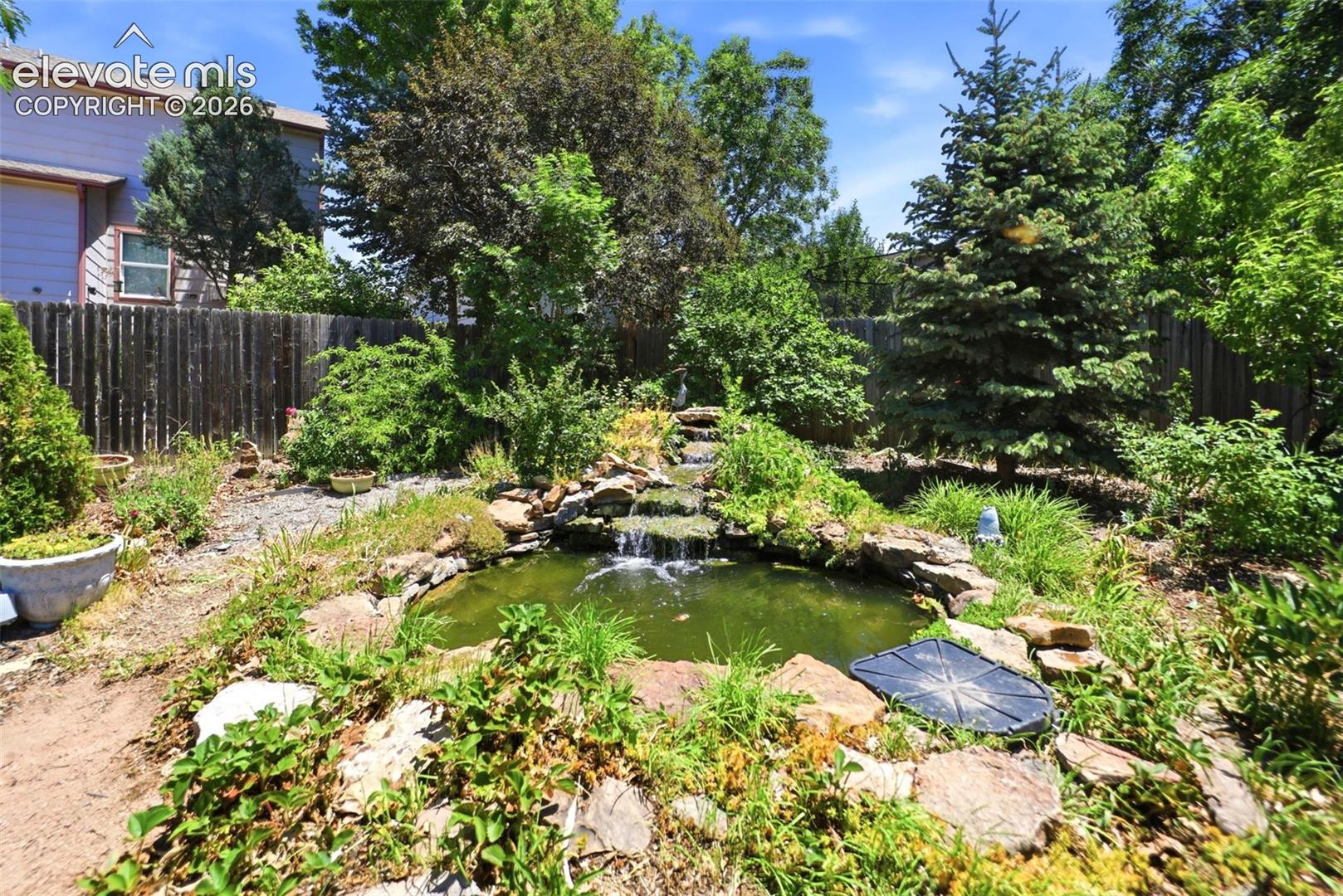 Landscaped backyard featuring a multi-tiered rock waterfall and pond