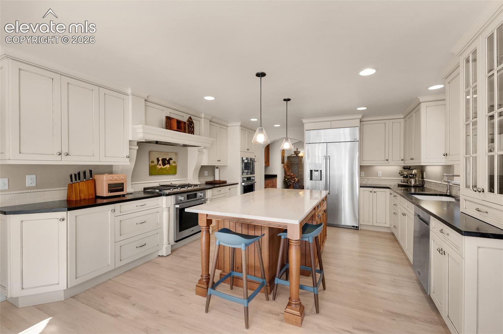 Custom cabinetry with glass-front display uppers, center island with stone countertop, stainless steel appliances, recessed lighting, and wood-finish flooring
