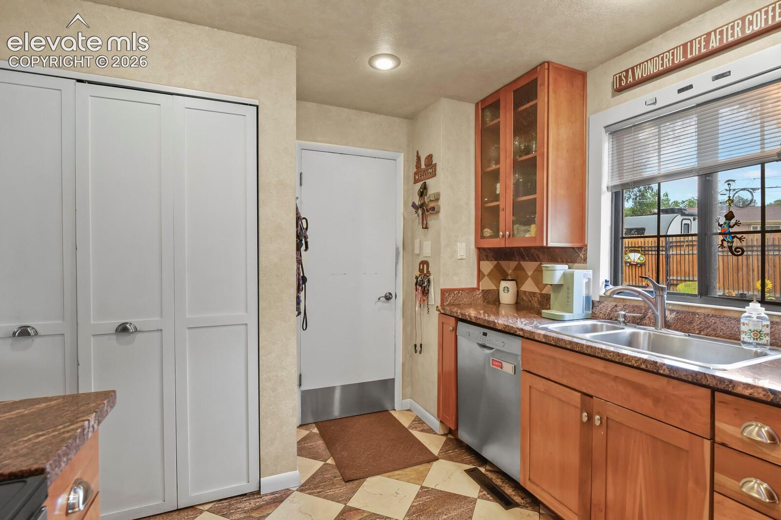 Wood-finish cabinetry with glass-front uppers, stainless steel dishwasher, double basin sink with chrome faucet, and patterned tile backsplash
