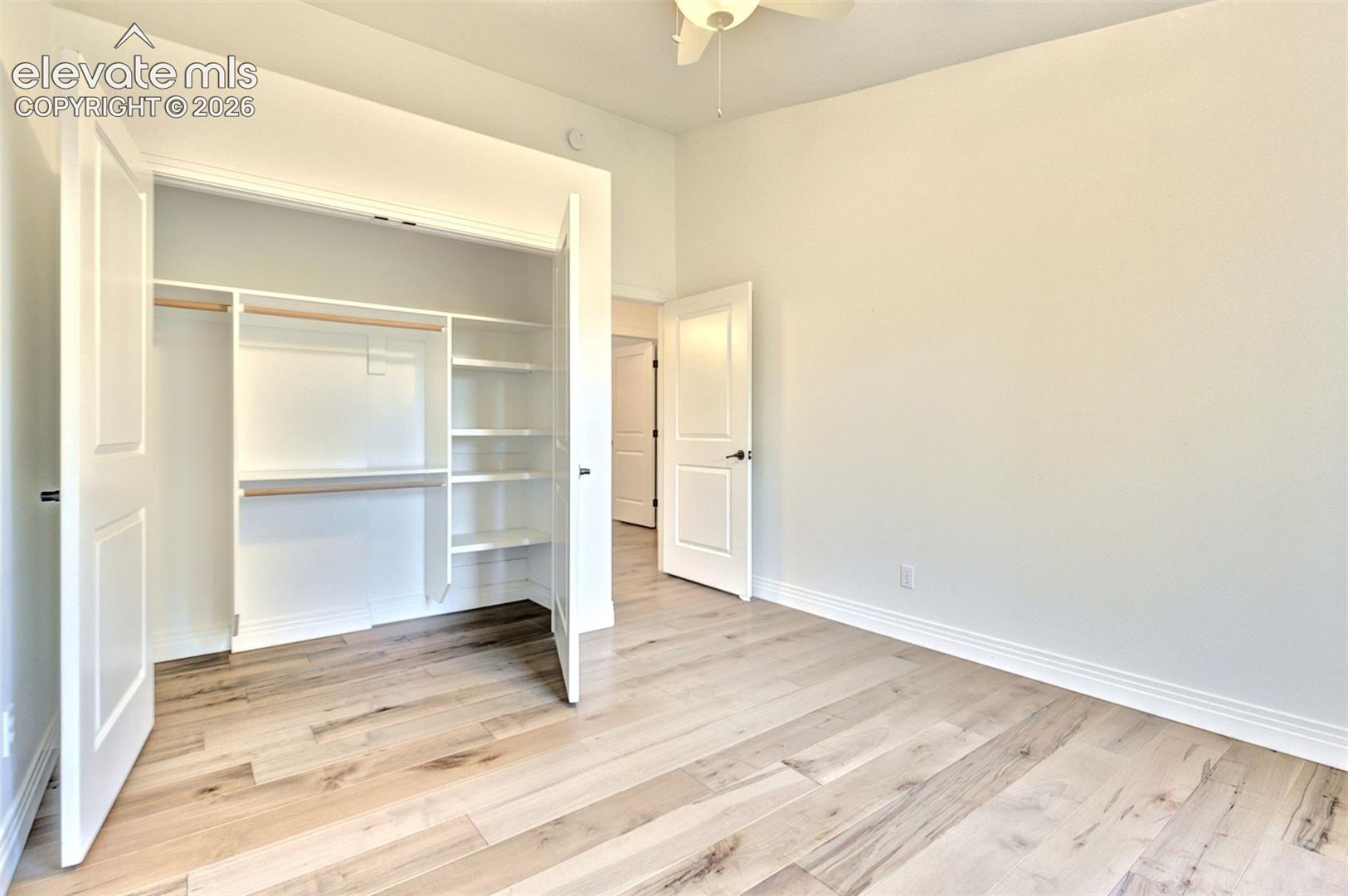 Wood-finish flooring, high ceilings with a built-in ceiling fan, and a custom closet system featuring integrated shelving and hanging rods