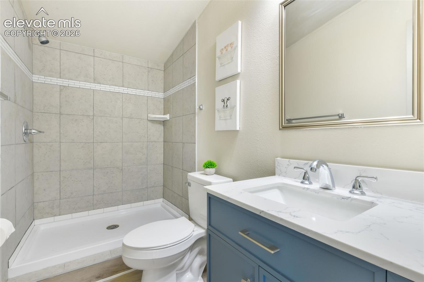 Vanity with a white countertop and undermount sink, chrome faucet, framed mirror, and tiled shower with a mosaic accent band