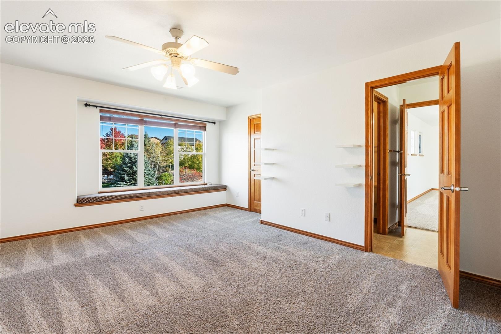 Room featuring neutral carpeting, a built-in window seat, multi-pane windows, a ceiling fan with light fixture, and wooden interior doors