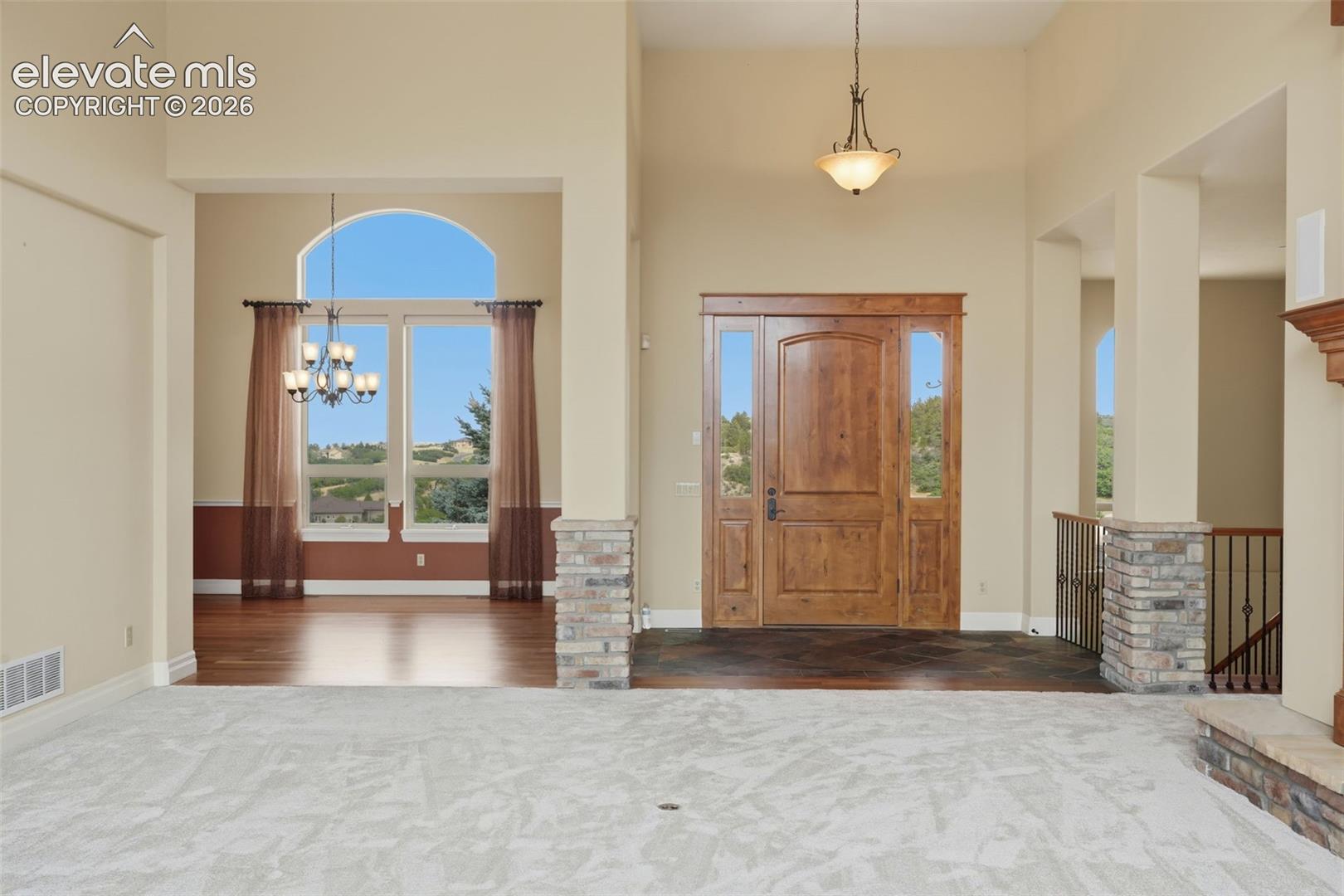 Two-story entryway featuring a natural wood front door with sidelights, a large arched window, a chandelier, and a stone-clad column