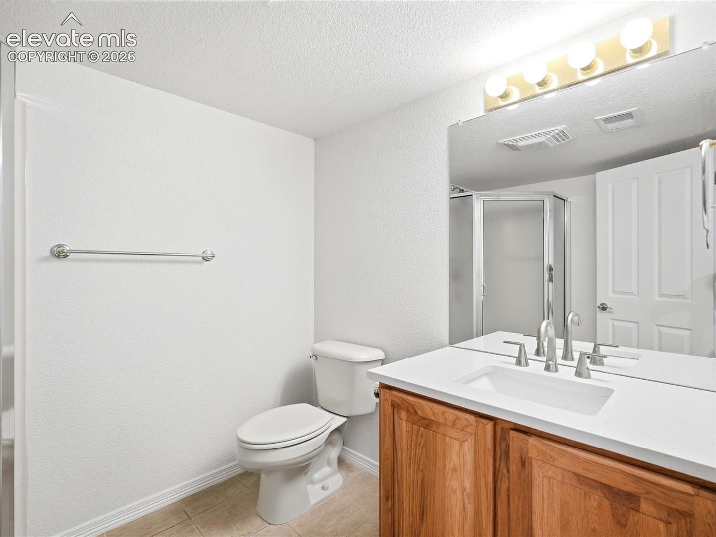 Bathroom vanity featuring a light-toned countertop, undermount sink, wood-finish cabinetry, and a full-width mirror with integrated lighting