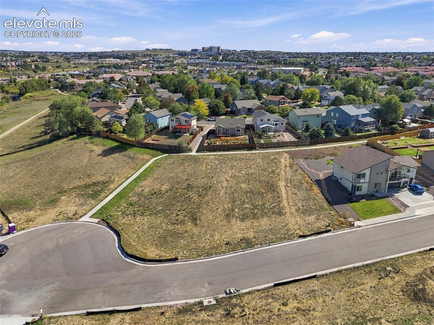 Expansive lot featuring a curvilinear paved road, a concrete sidewalk, and surrounding residential structures