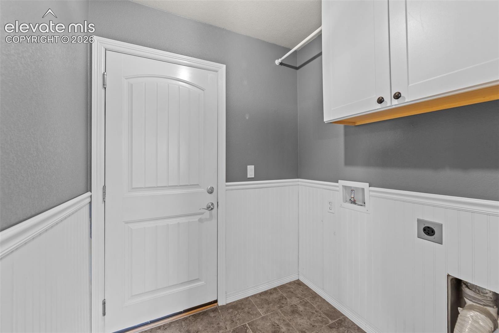 White wainscoting with decorative trim, durable flooring, white storage cabinetry, and a clothing rod