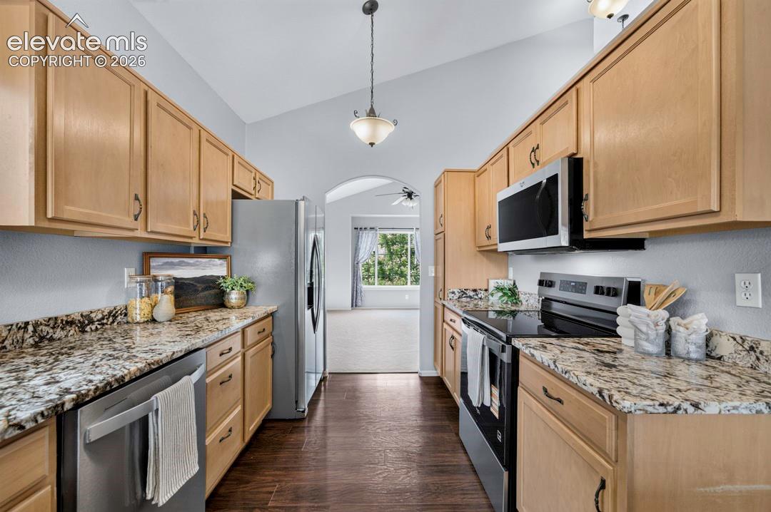 Kitchen featuring light wood cabinetry, stone countertops, stainless steel appliances, dark wood-finish flooring, and a vaulted ceiling