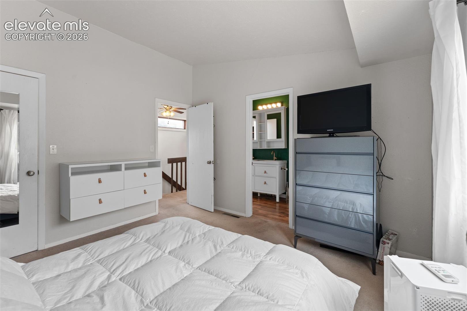 Carpeted room with a wall-mounted dresser, an attached bathroom featuring a vanity with a rectangular sink, and wood-finish flooring