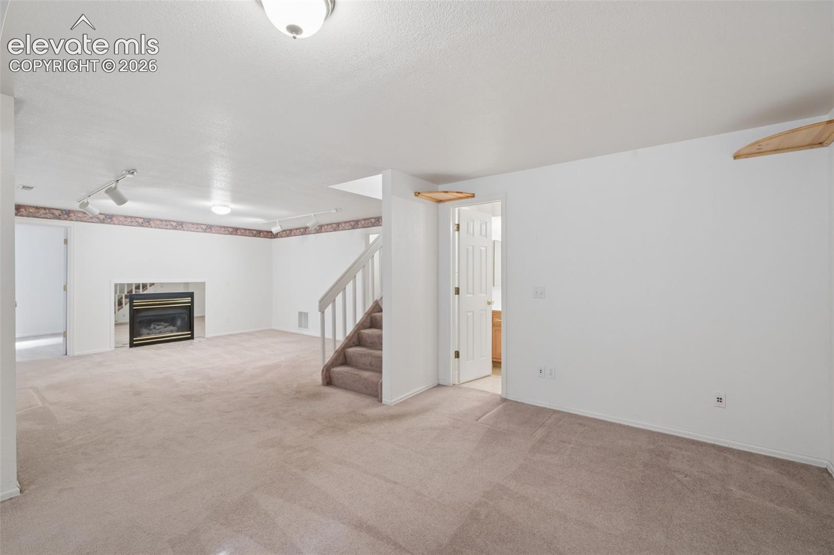 Open-concept interior featuring wall-to-wall carpeting, a recessed fireplace with a black surround, a central staircase with a white balustrade, and adjustable track lighting