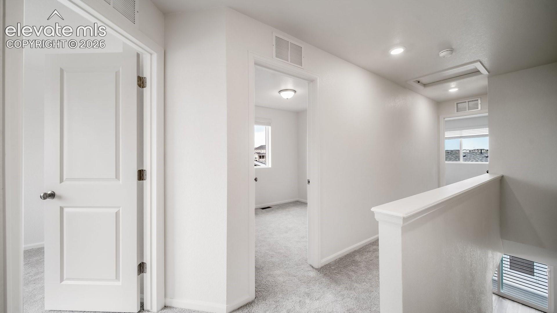 Carpeted hallway with white walls, recessed lighting, white doors, and a white stair railing
*photos of a model home*