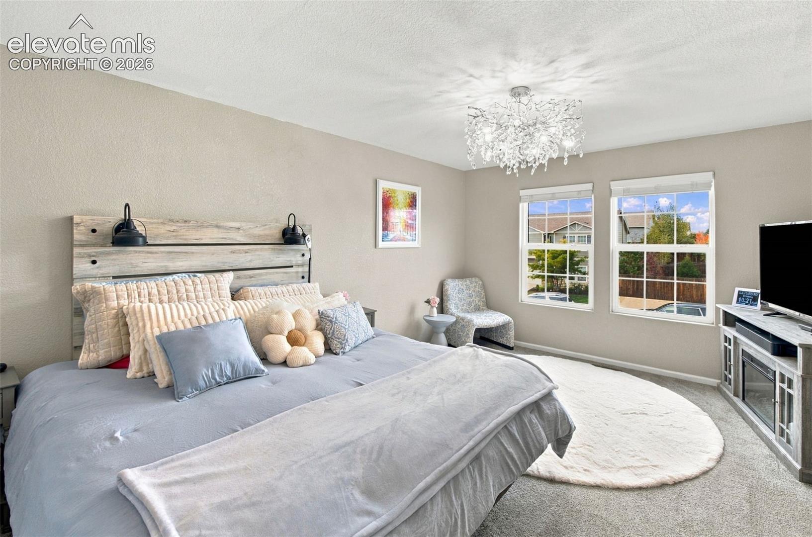 Bedroom featuring neutral wall paint, two dual-pane windows, carpeted flooring, and a decorative crystal-style chandelier