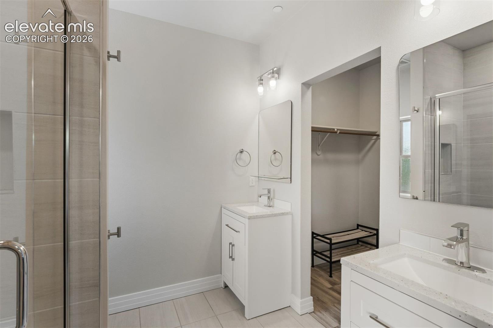 Ensuite bathroom with dual vanities, walk in shower, and walk in closet