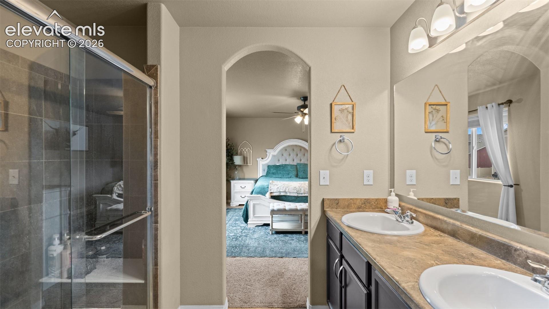 Bathroom featuring a dual-sink vanity with a laminate countertop, an expansive mirror, and a glass-enclosed shower with tiled walls and a built-in shelf