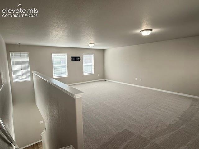 Spacious room featuring carpeting, multiple windows with blinds, a partial railing, and flush-mount lighting fixtures