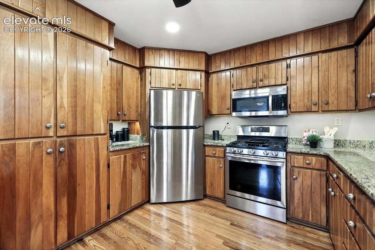 Kitchen featuring wood-paneled cabinetry, stone countertops, and stainless steel appliances including a gas range and built-in microwave