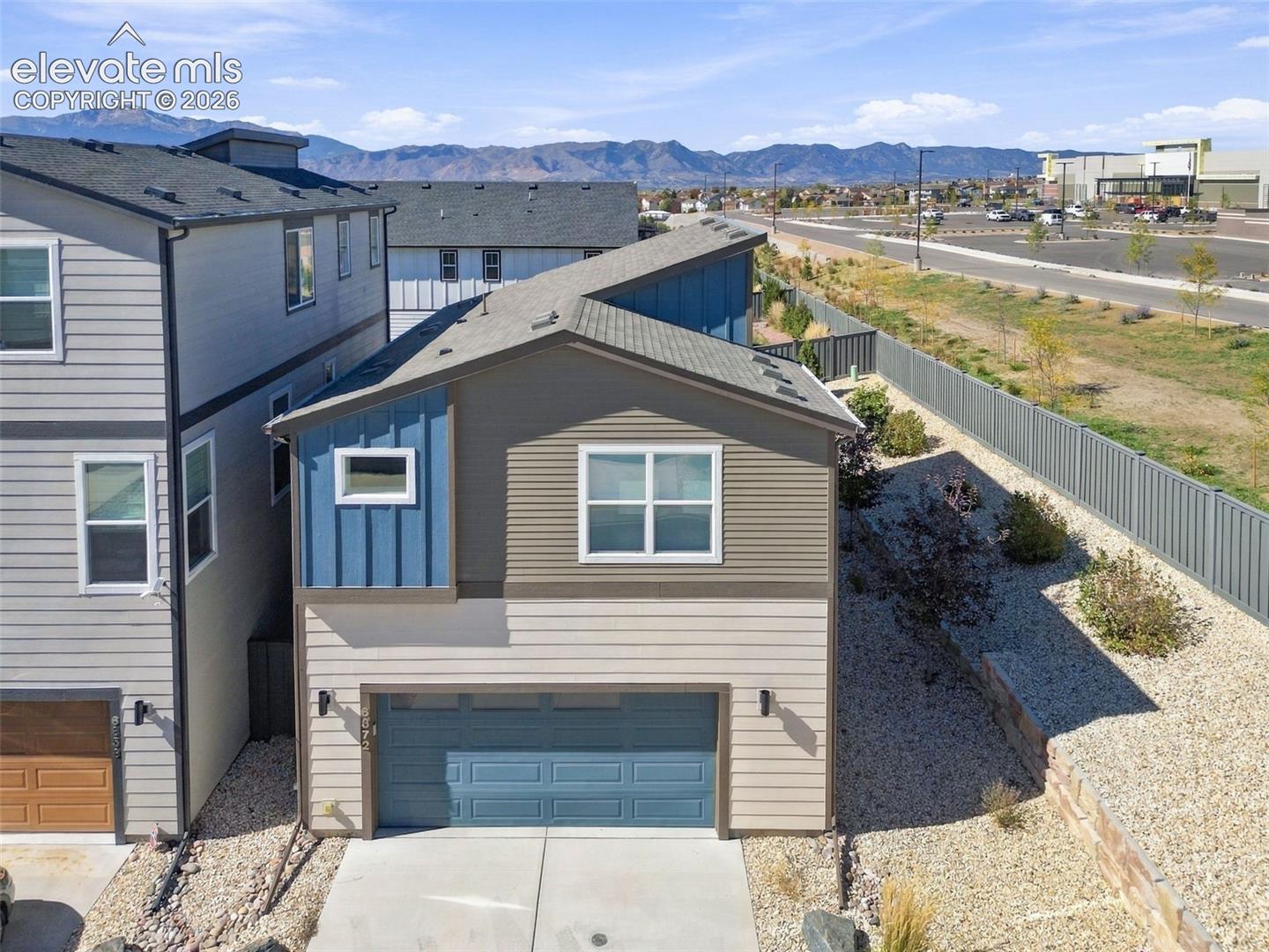 Two-story residence featuring multi-tone horizontal siding, vertical paneling accents, an attached two-car garage, and mountain-range scenery