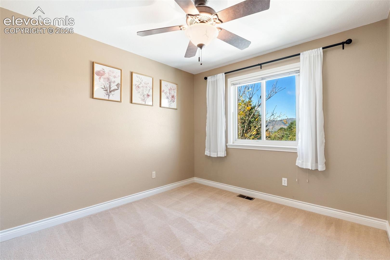Neutral-toned interior featuring wall-to-wall carpeting, a ceiling fan with integrated lighting, and a window with exterior mountain scenery