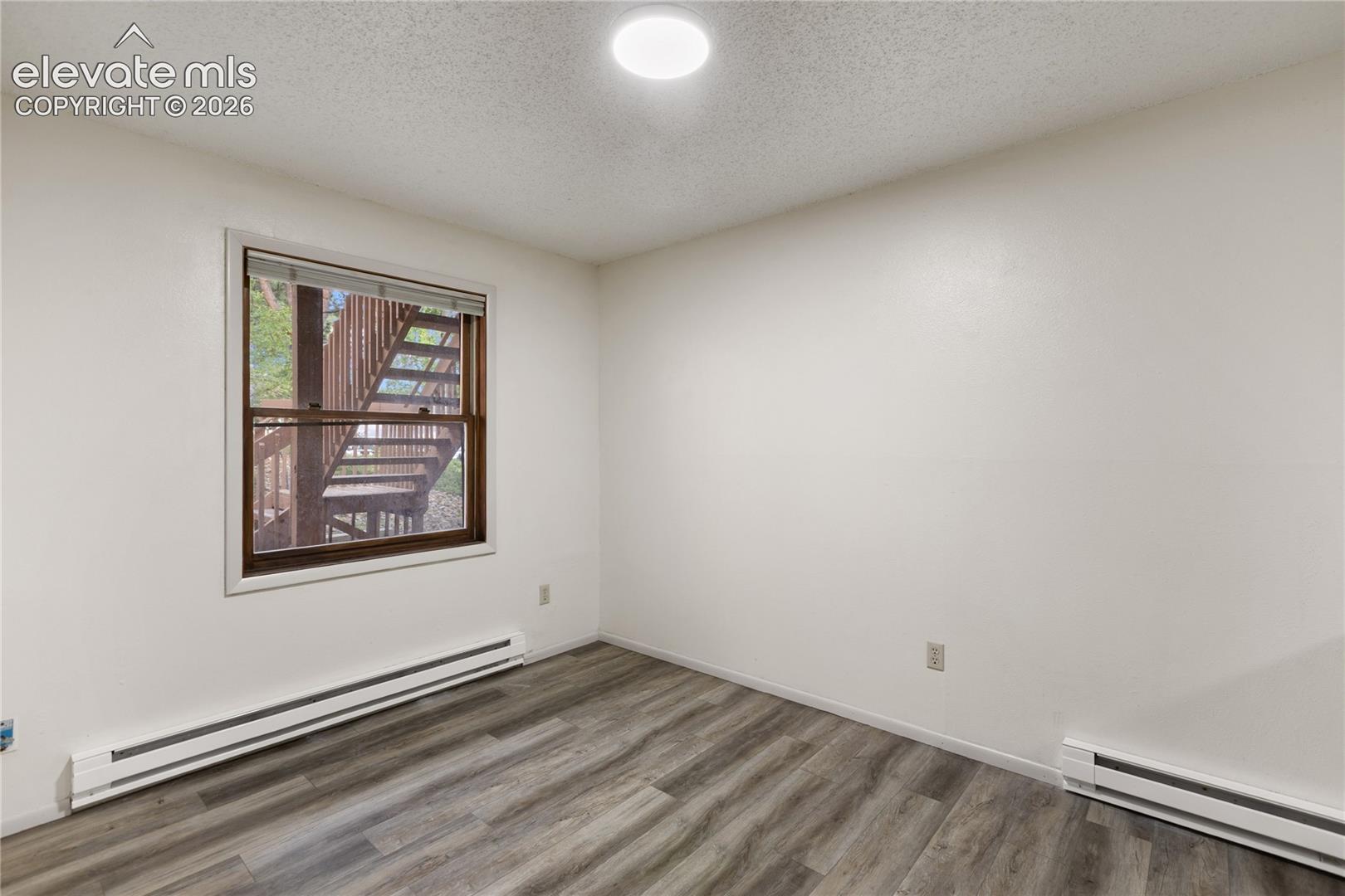 Room featuring wood-finish flooring, a window with exterior stair access, white walls, and a flush-mount ceiling light