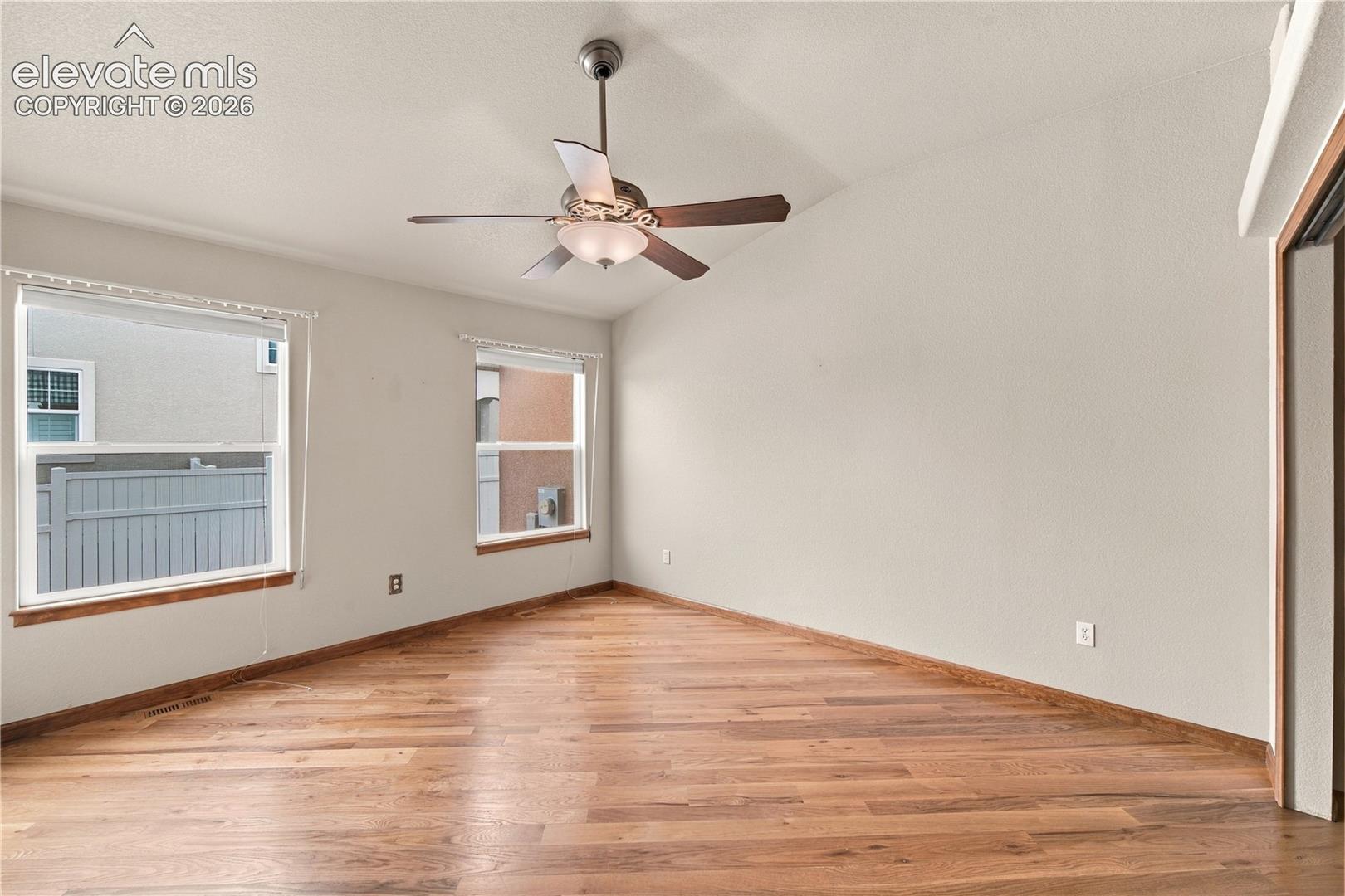 Room featuring wood-finish flooring, dual windows with wood trim, and a ceiling-mounted fan with integrated lighting