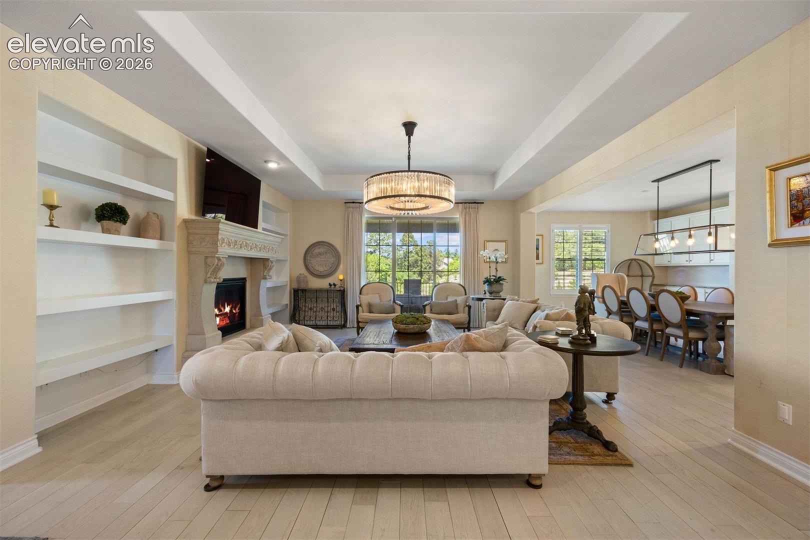 Spacious living area featuring light wood-finish flooring, a decorative fireplace with an ornate stone surround, and built-in shelving