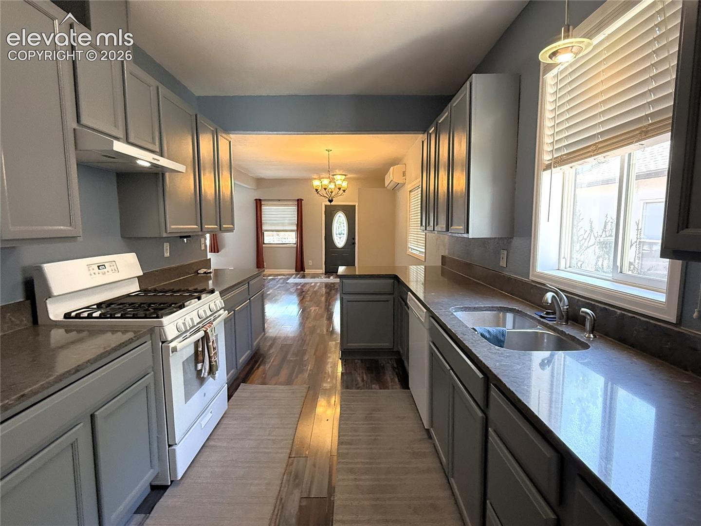 Kitchen featuring grey shaker-style cabinetry, solid-surface countertops, dual-basin stainless steel sink, gas range, and wood-finish flooring