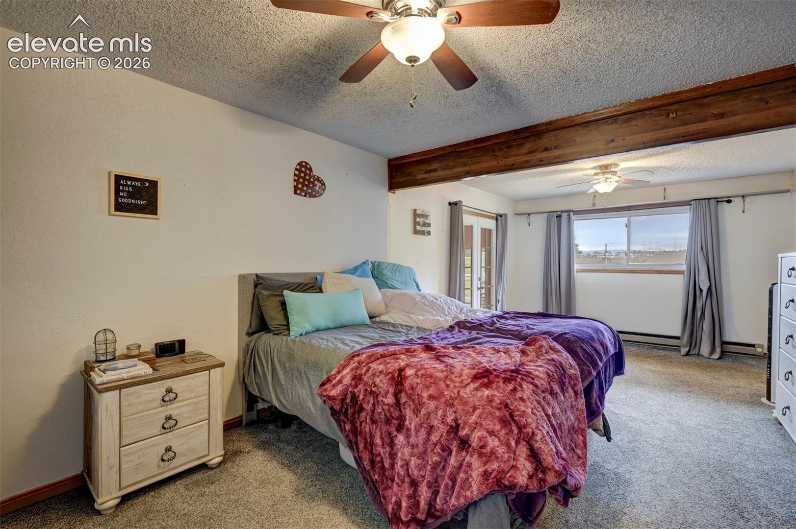 Carpeted flooring, exposed wood beam, ceiling fan with integrated lighting, glass-paned double doors, and a large window