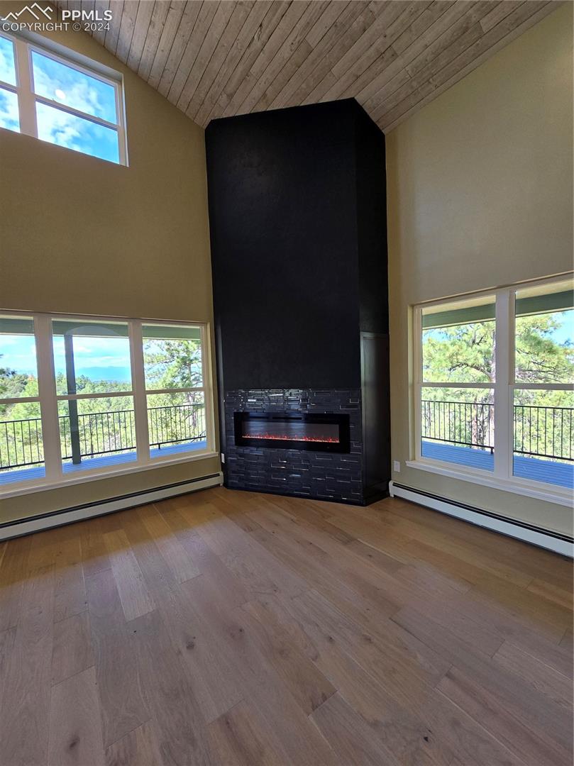 Unfurnished living room with wooden ceiling, a healthy amount of sunlight, wood-type flooring, and contrmporary electric fireplace