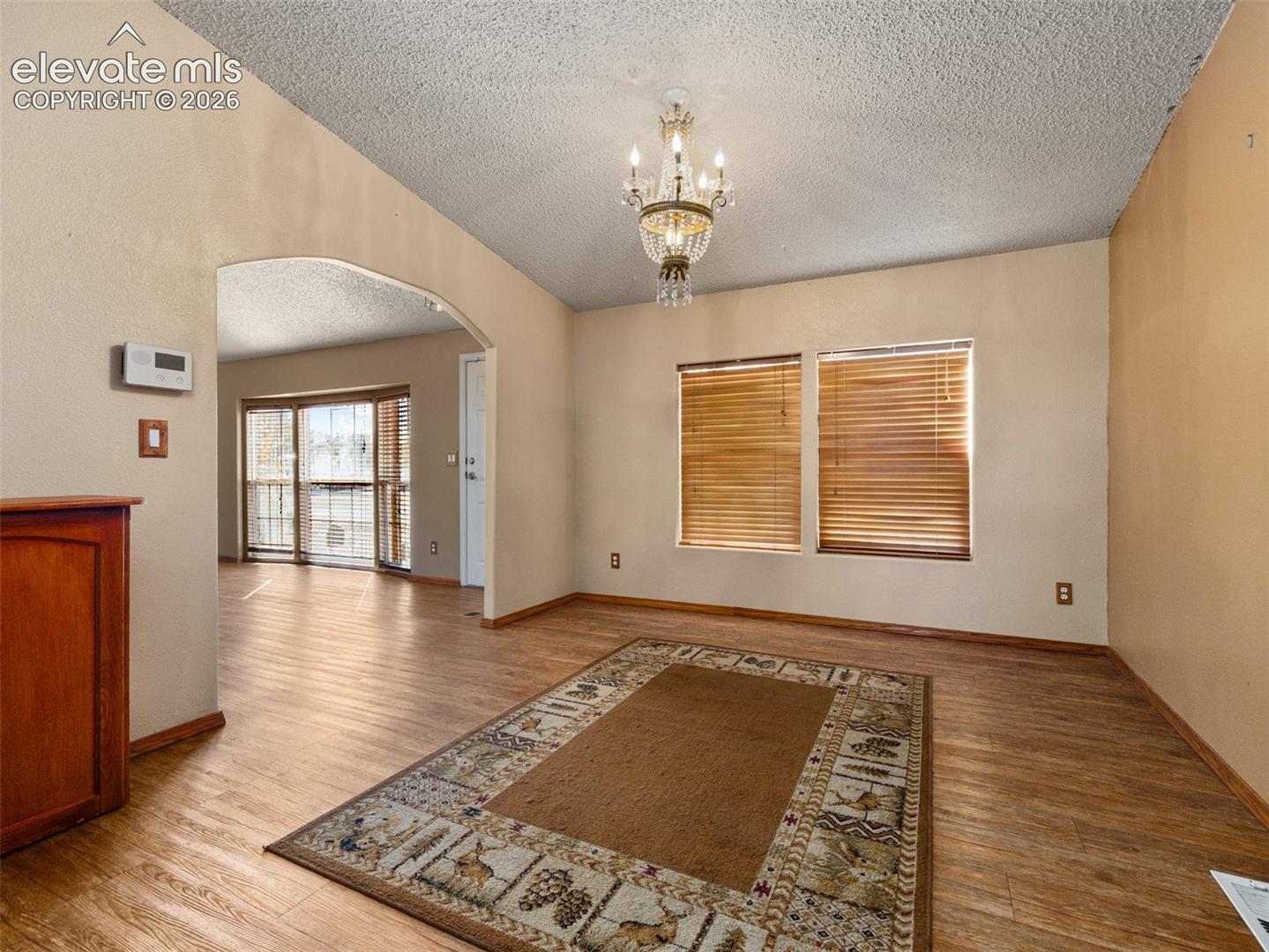 Vaulted ceiling featuring a classic crystal chandelier, wood-finish flooring, and an arched architectural opening