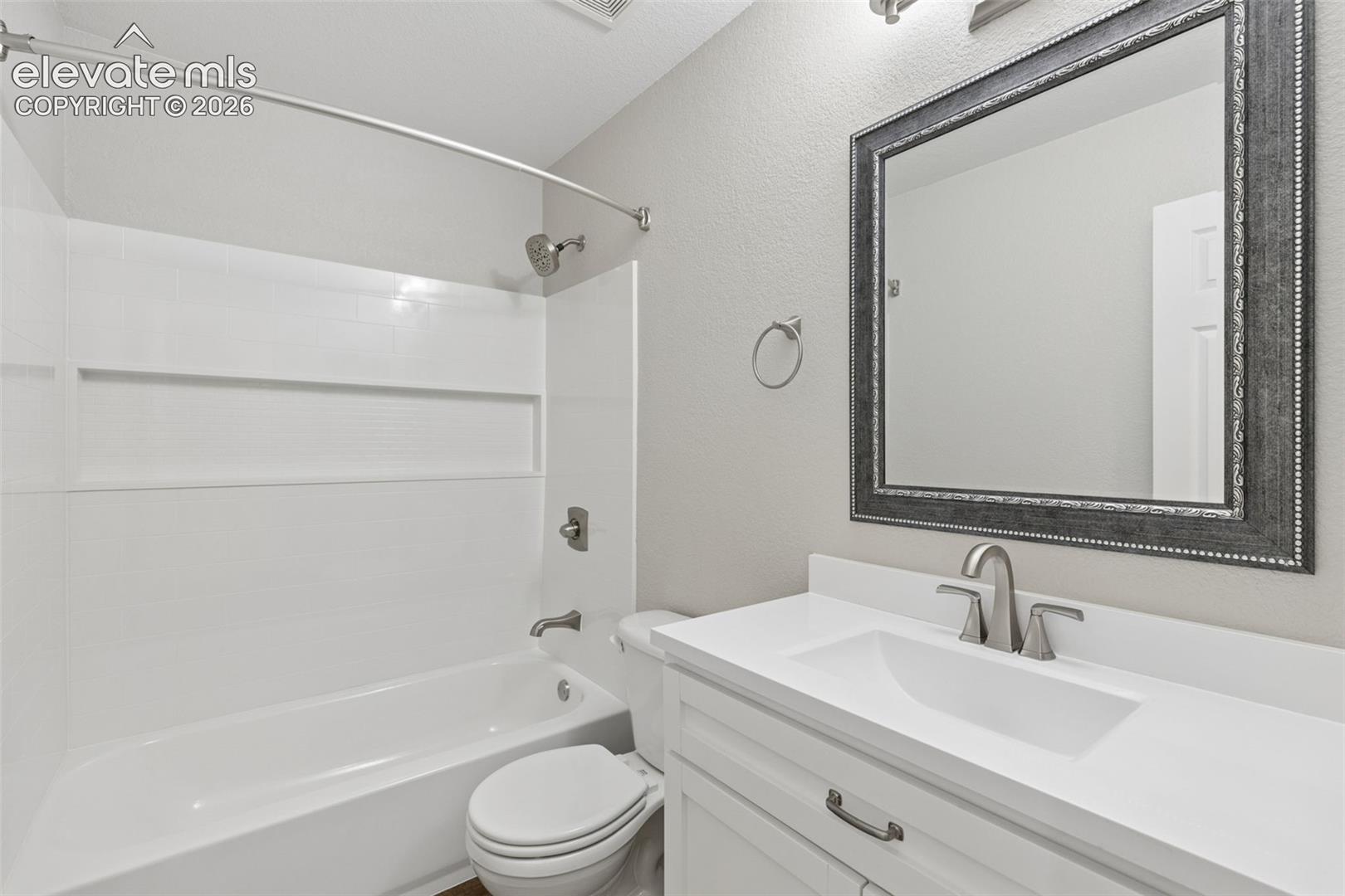 White vanity with a rectangular sink, brushed nickel faucet, solid surface countertop, and built-in bathtub with a white surround and chrome hardware