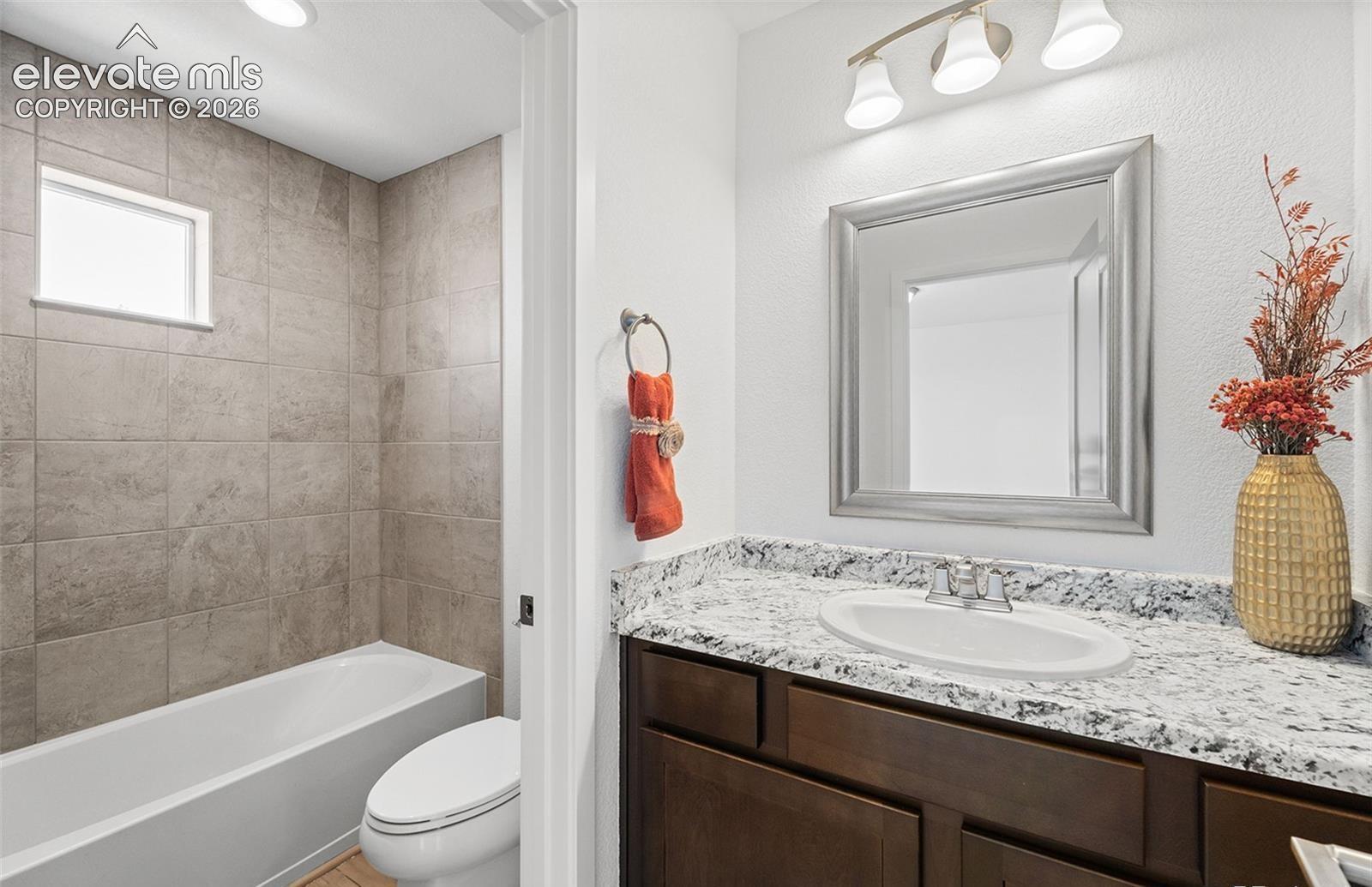 Bathroom featuring a vanity with dark-finish cabinetry, a stone-composite countertop, an integrated oval basin, and a framed mirror under three-light fixture vanity lighting