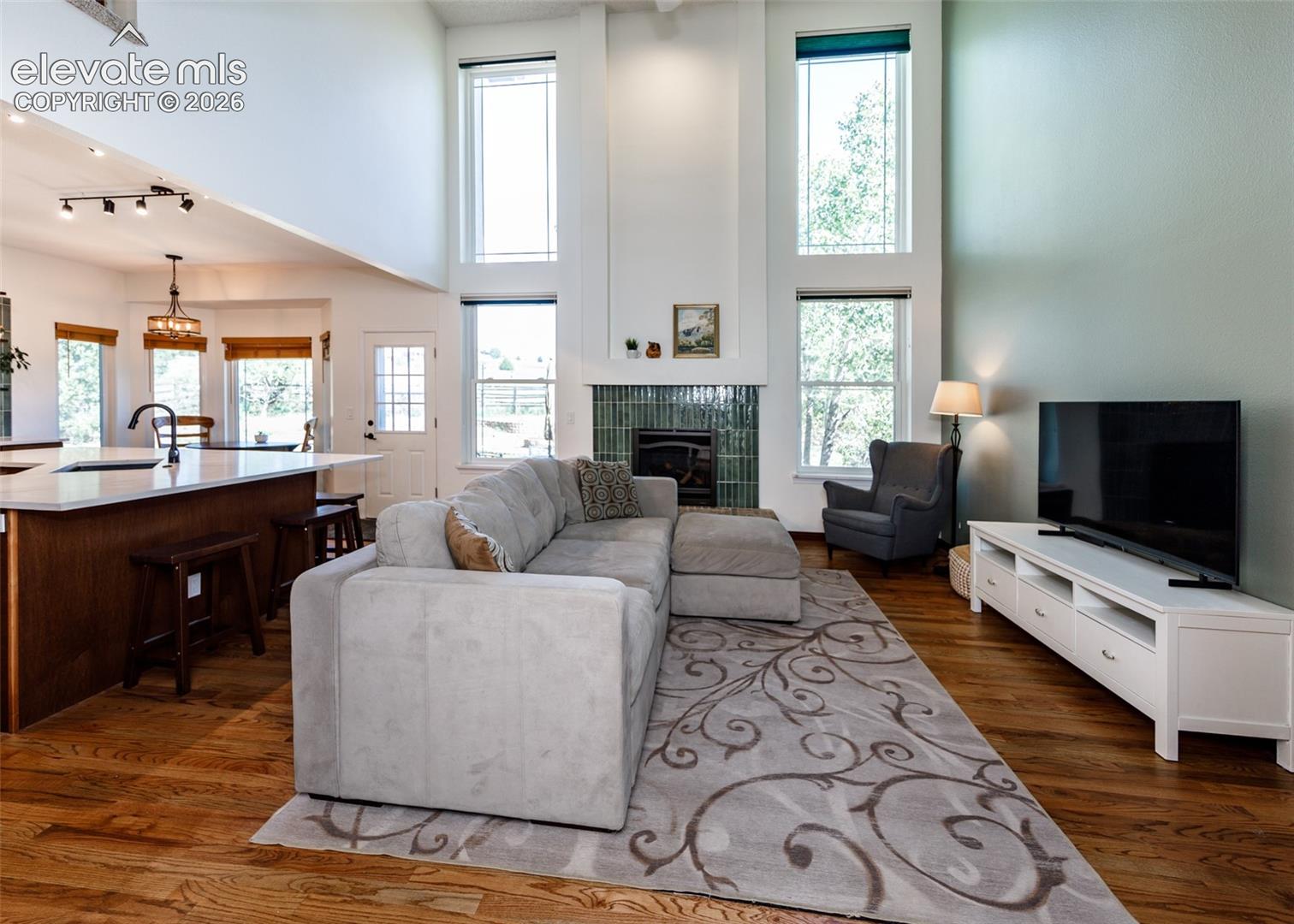 Vaulted ceilings, wood-finish flooring, a kitchen island with seating, a fireplace featuring a tile surround, and tall windows