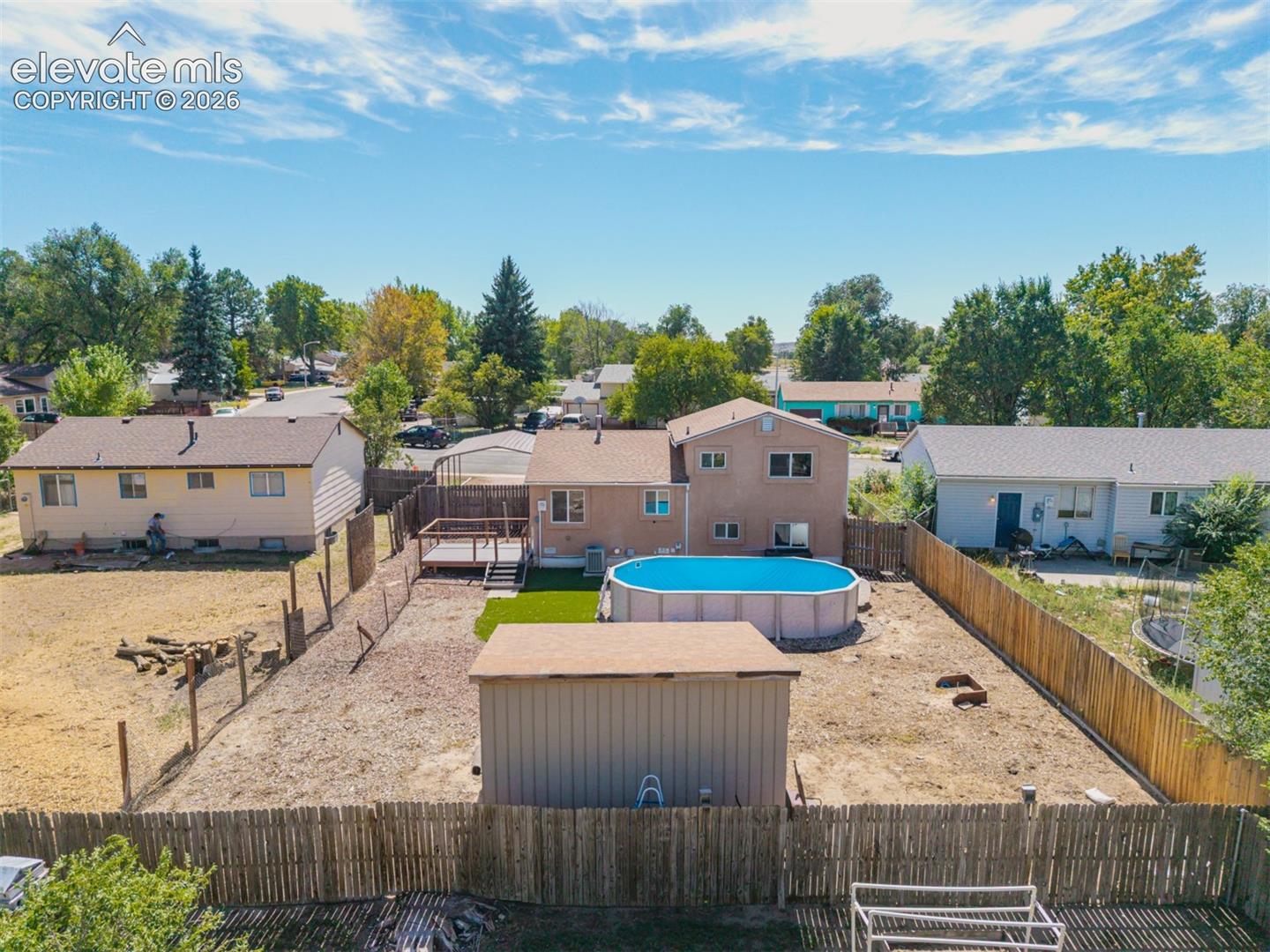 Aerial view of expansive backyard featuring a privacy fence, above-ground pool, storage shed, and a deck